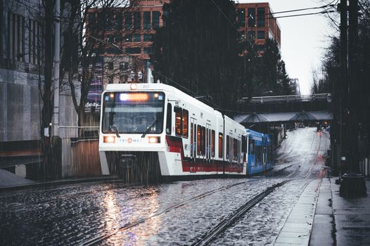 Tram moving along cobbled street with reflection of light of headlights in wet surface in daytime during overcast