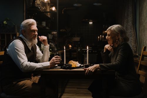 Free An elderly couple sharing a romantic dinner with candles and wine in a cozy room. Stock Photo