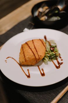 Close-up of a delicious grilled salmon steak with sauce and greens on a white plate.