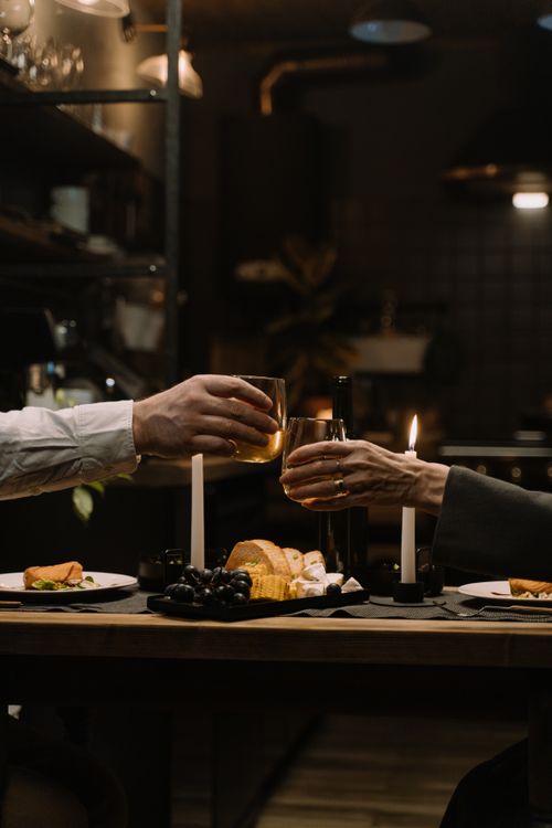 Free Cozy candlelit dinner setting with glasses raised for a toast, capturing a moment of celebration and intimacy. Stock Photo