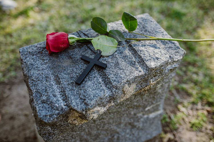 Black Cross And A Stem Of Rose On Gray Concrete Stone