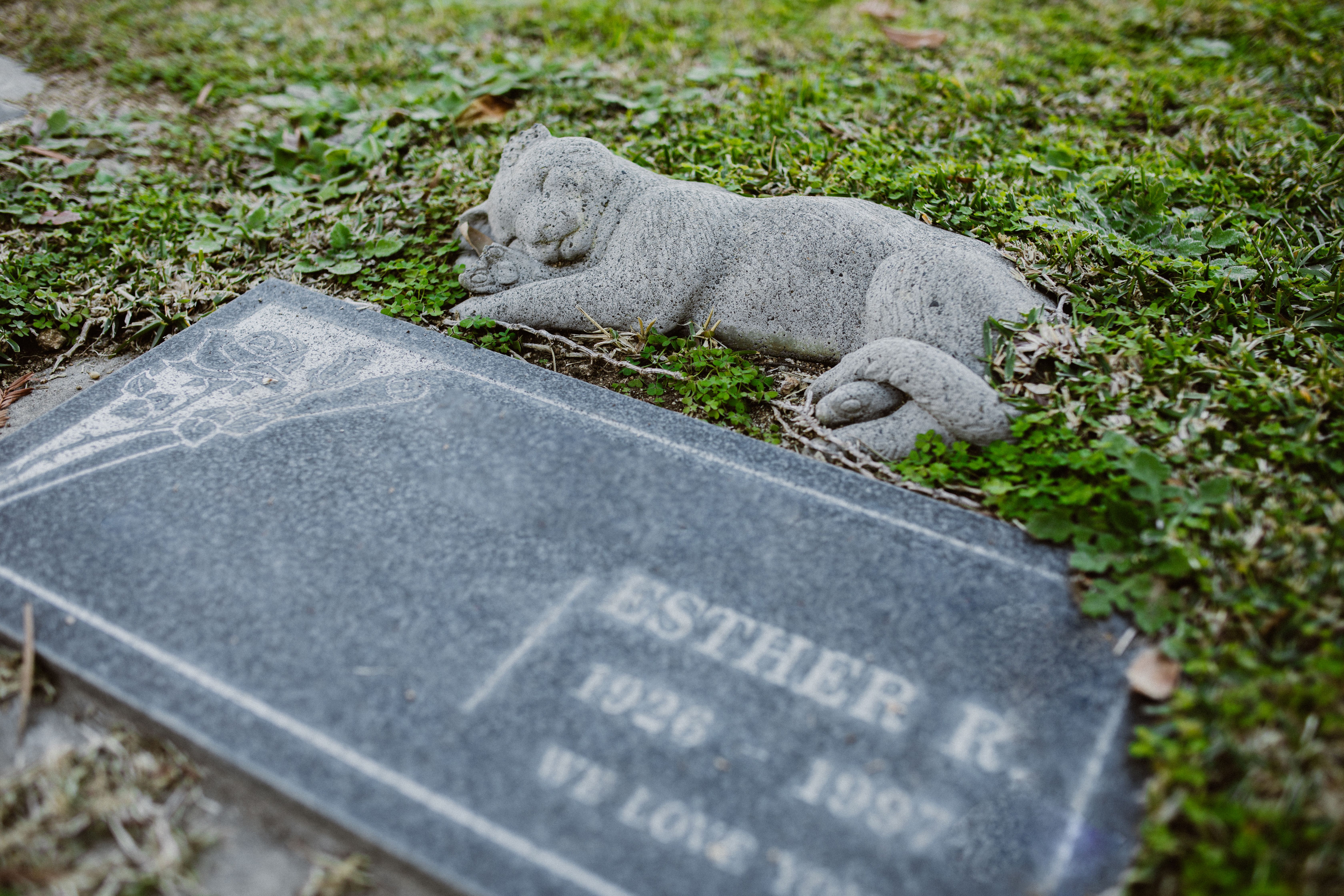 Memorial stones for dogs: a flat gray stone grave marker set level in green grass beside a small stone figure