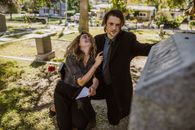 Man in Black Suit Jacket Sitting Beside Woman in Black and White Shirt and Black Pants