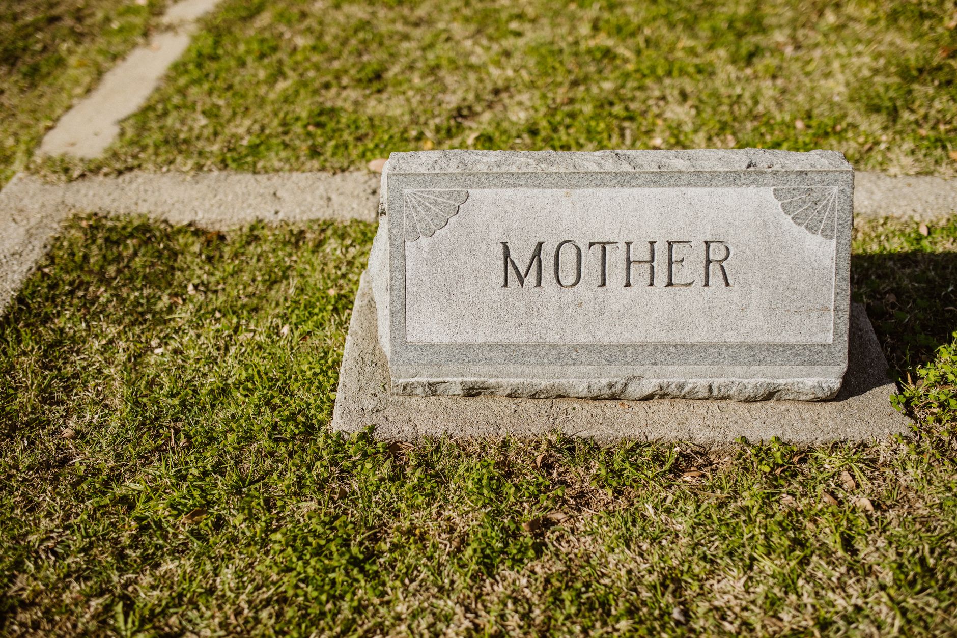 Gravestone in cemetery engraved with the word 'Mother' on grass.