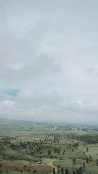 Expansive view of rolling countryside under a cloudy sky, featuring lush cropland and natural beauty.