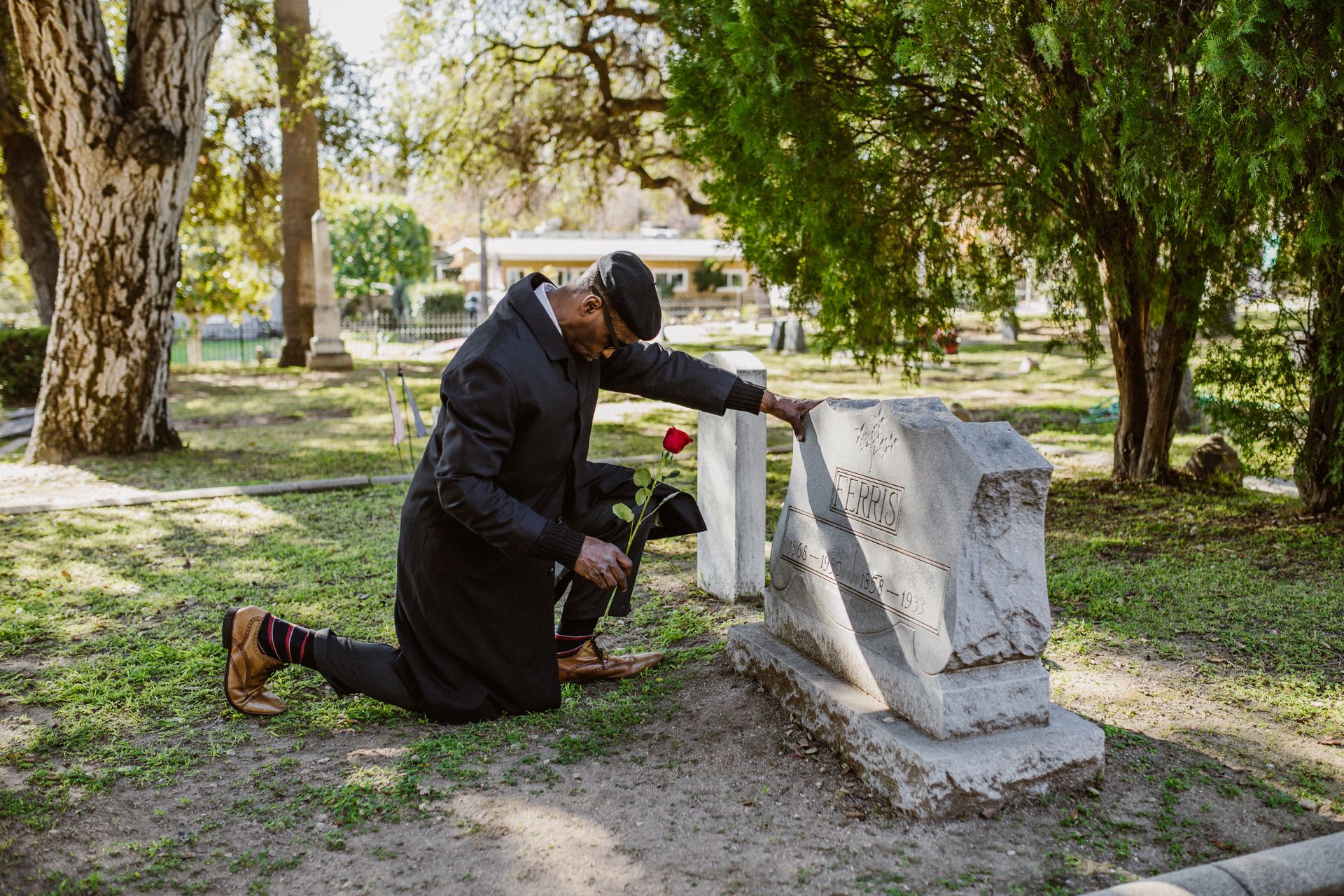 A Man in Black Clothes Kneeling Before a Tombstone