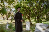 A man stands in a cemetery holding a red rose, symbolizing bereavement.