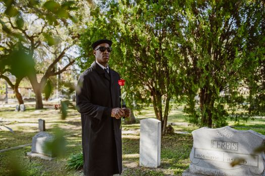 A man stands in a cemetery holding a red rose, symbolizing bereavement.