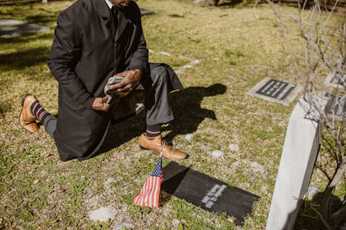 A Man Kneeling In Front of a Gravestone