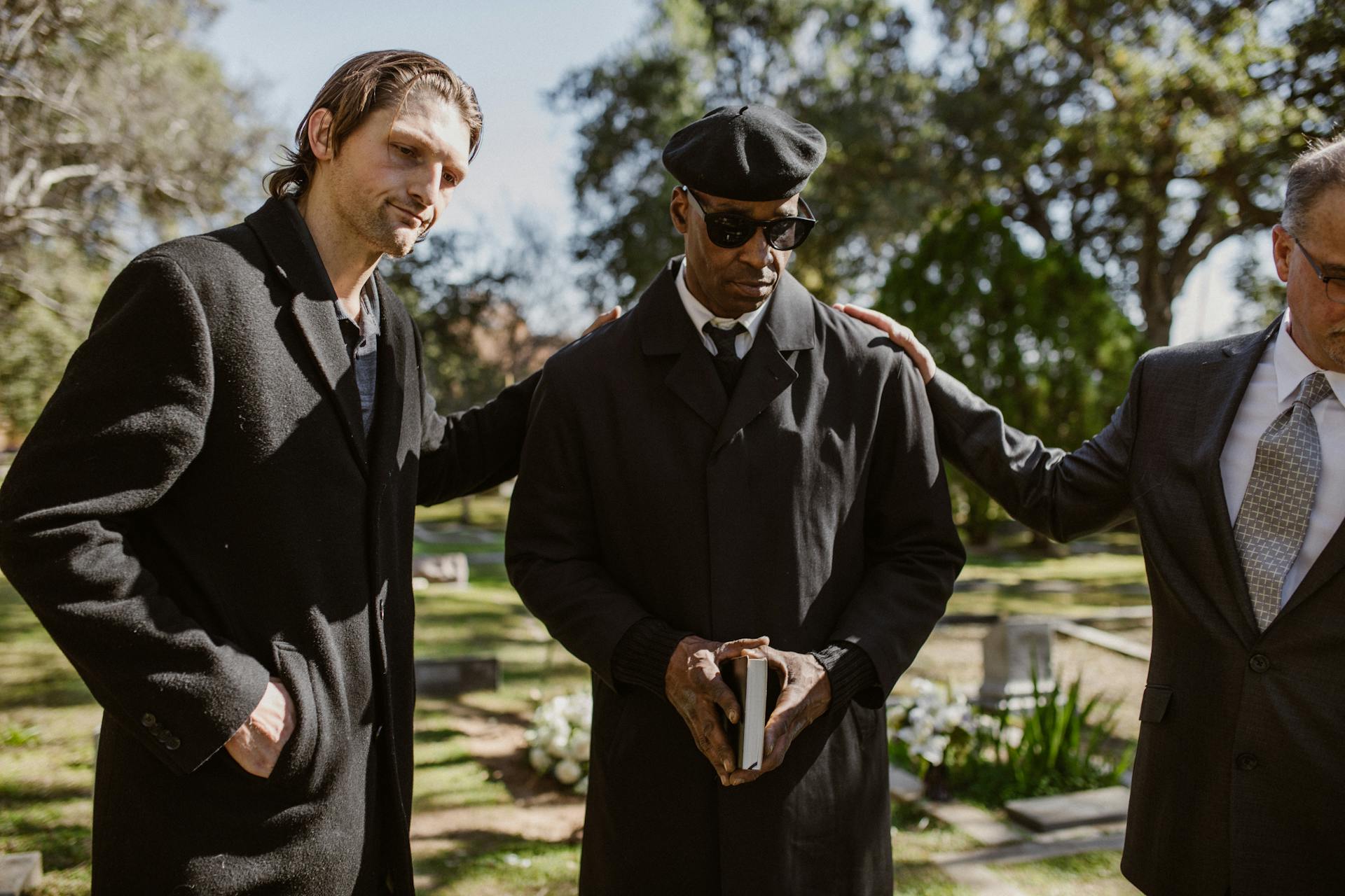 Men in black coats standing together during a somber outdoor funeral service.