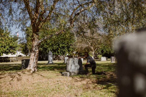 Free Man Crouching in Front of a Grave at Cemetery Stock Photo