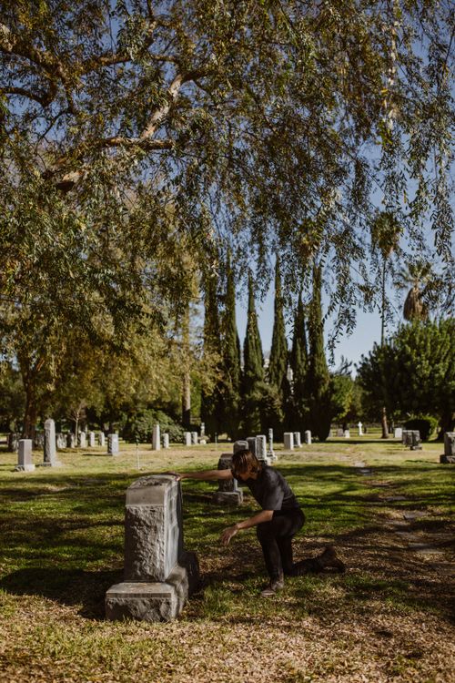 Free A man mourning at a gravestone in a peaceful cemetery surrounded by trees. Stock Photo