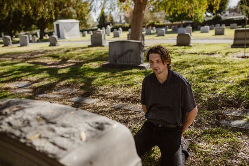 Free A man kneels at a grave in a sunlit cemetery, expressing grief and remembrance. Stock Photo