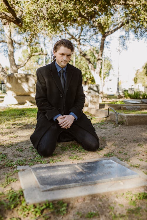 Free Lonely Man in Black Suit Kneeling in Front of a Grave in Cemetery Stock Photo
