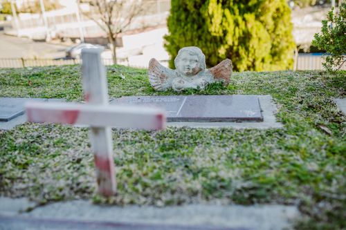 Free A tranquil cemetery view featuring a stone cross and angel sculpture on a grassy grave. Stock Photo
