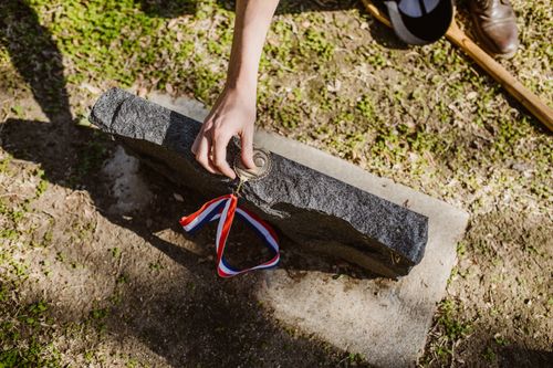 Free A hand placing a medal on a tombstone in a grassy cemetery, symbolizing honor and remembrance. Stock Photo