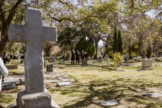 A tranquil scene in a cemetery with a family gathering among tombstones and sunlit trees.