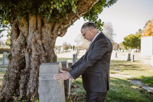 Photo of Elderly Man touching a Gravestone
