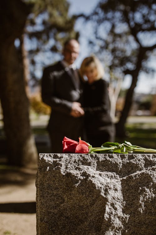Man and Woman Standing on Grave with Flower on Tombstone