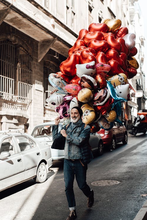 Free Content ethnic male seller with assorted balloons walking on urban roadway while looking forward on Valentines Day Stock Photo