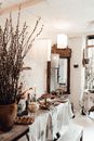Sprigs of osier on rustic table with assorted tasty food and flaming candles under lamps in house