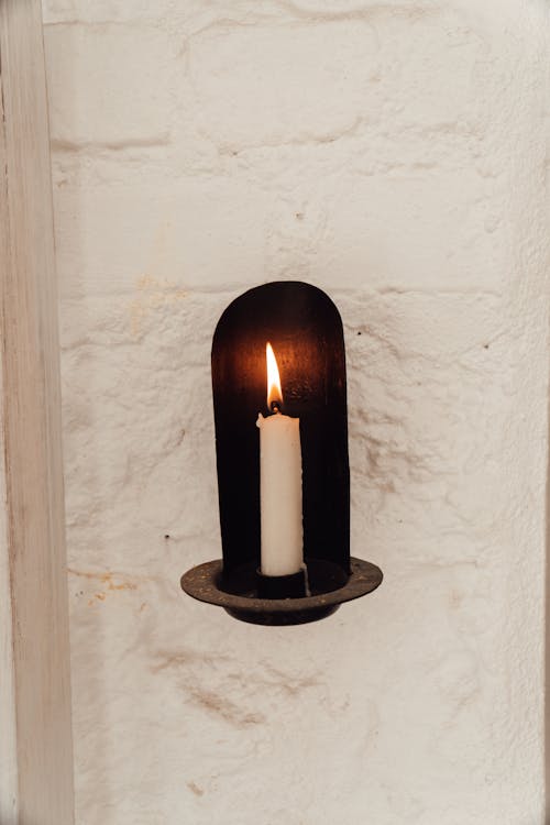 Burning candle in holder on rough wall