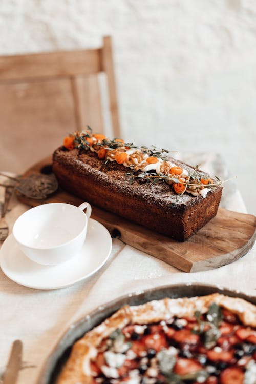 Free Tasty cake with carrot slices and thyme sprigs on chopping board against cup on table in house Stock Photo