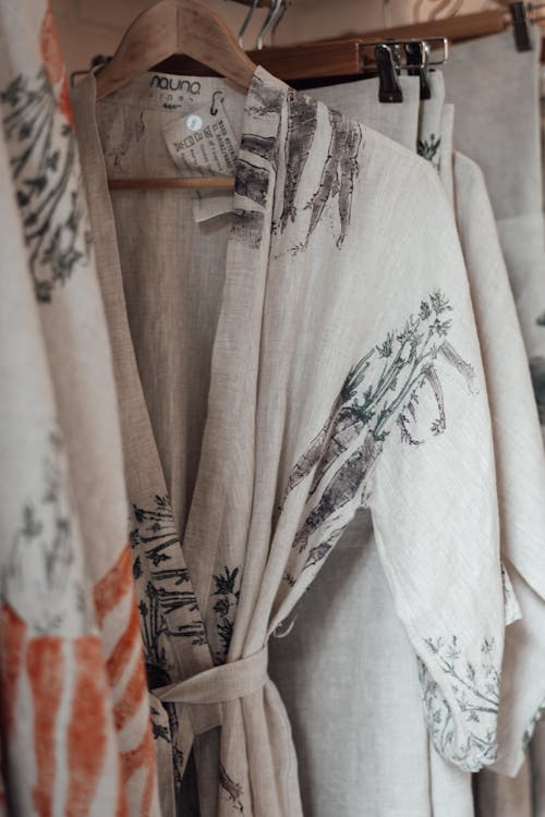 Assorted textiles and bathrobe with vegetable ornament and paper tag hanging on wooden rack in shop