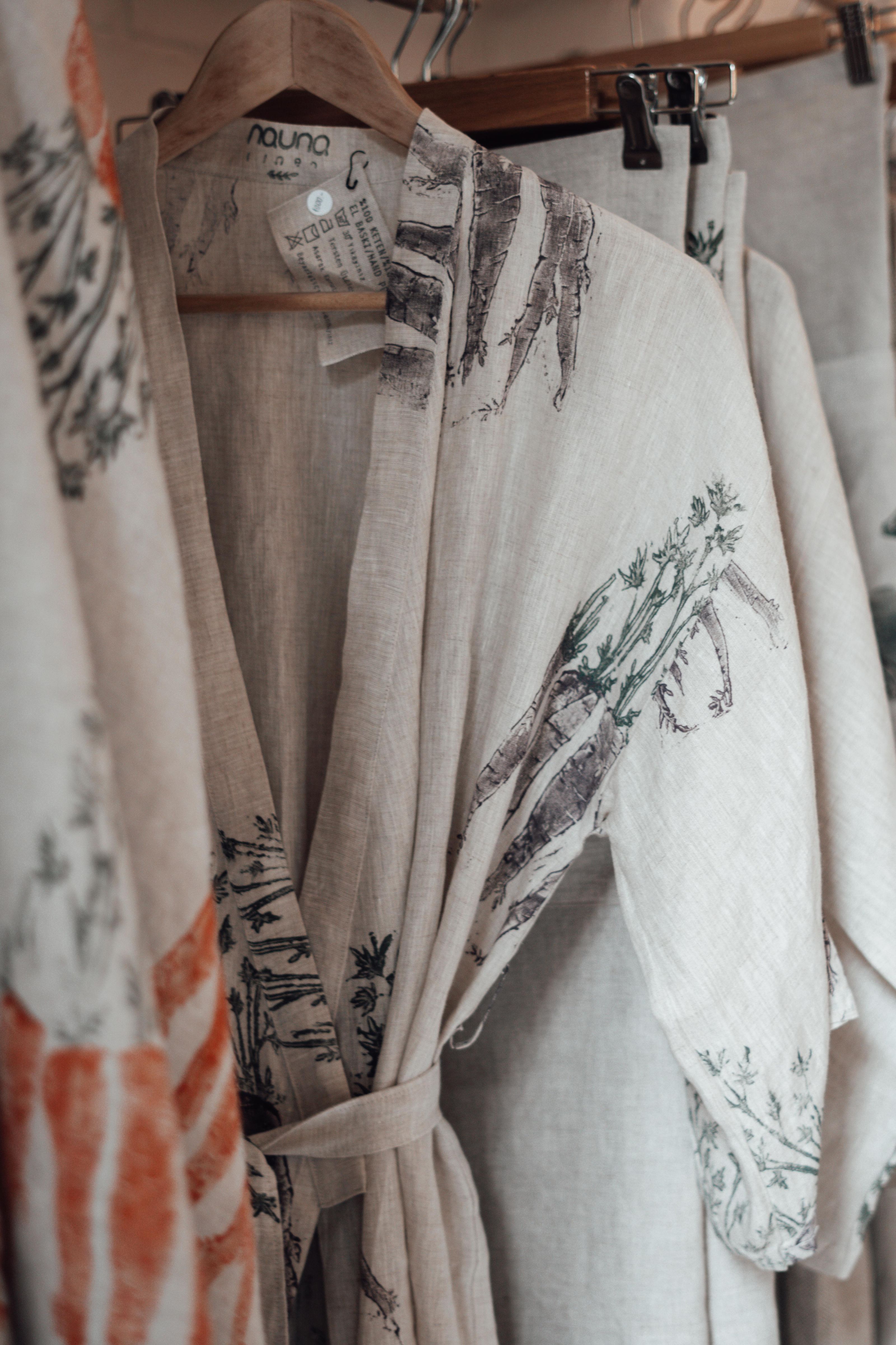 Roupões de linho estilosos com estampas botânicas pendurados em um ambiente aconchegante de boutique.