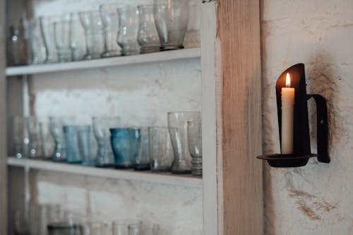 Flaming candle against shelves with glass vases indoors