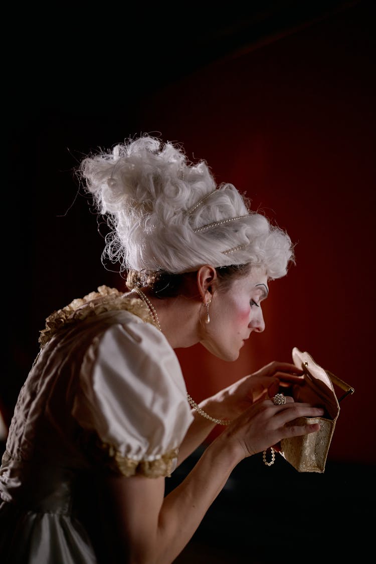 A Woman With A White Wig Looking Inside A Purse