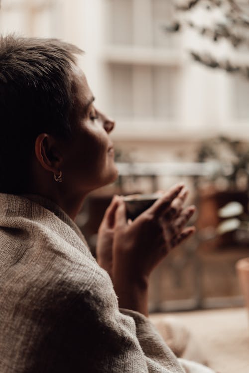 Crop dreamy woman enjoying coffee aroma on balcony