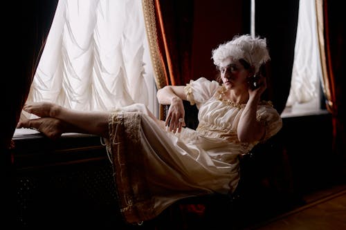 Free A Woman with White Wig Sitting on Chair with Feet on Window Sil Stock Photo