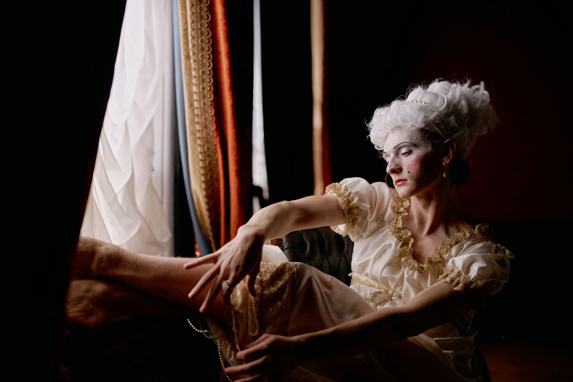 Dramatic portrait of a woman in historical costume by window, capturing elegant theatrical expression.