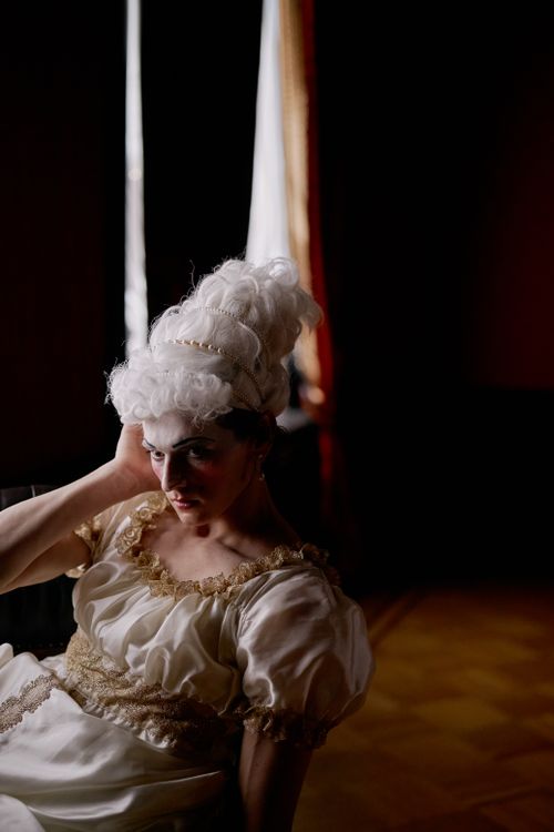 Free A woman in a period costume with a high, elaborate wig sits pensively in a dimly lit room. Stock Photo