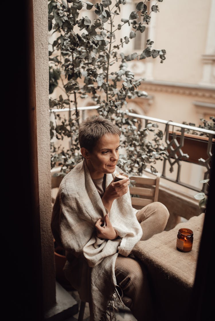 Woman In Plaid Blowing On Coffee On Balcony