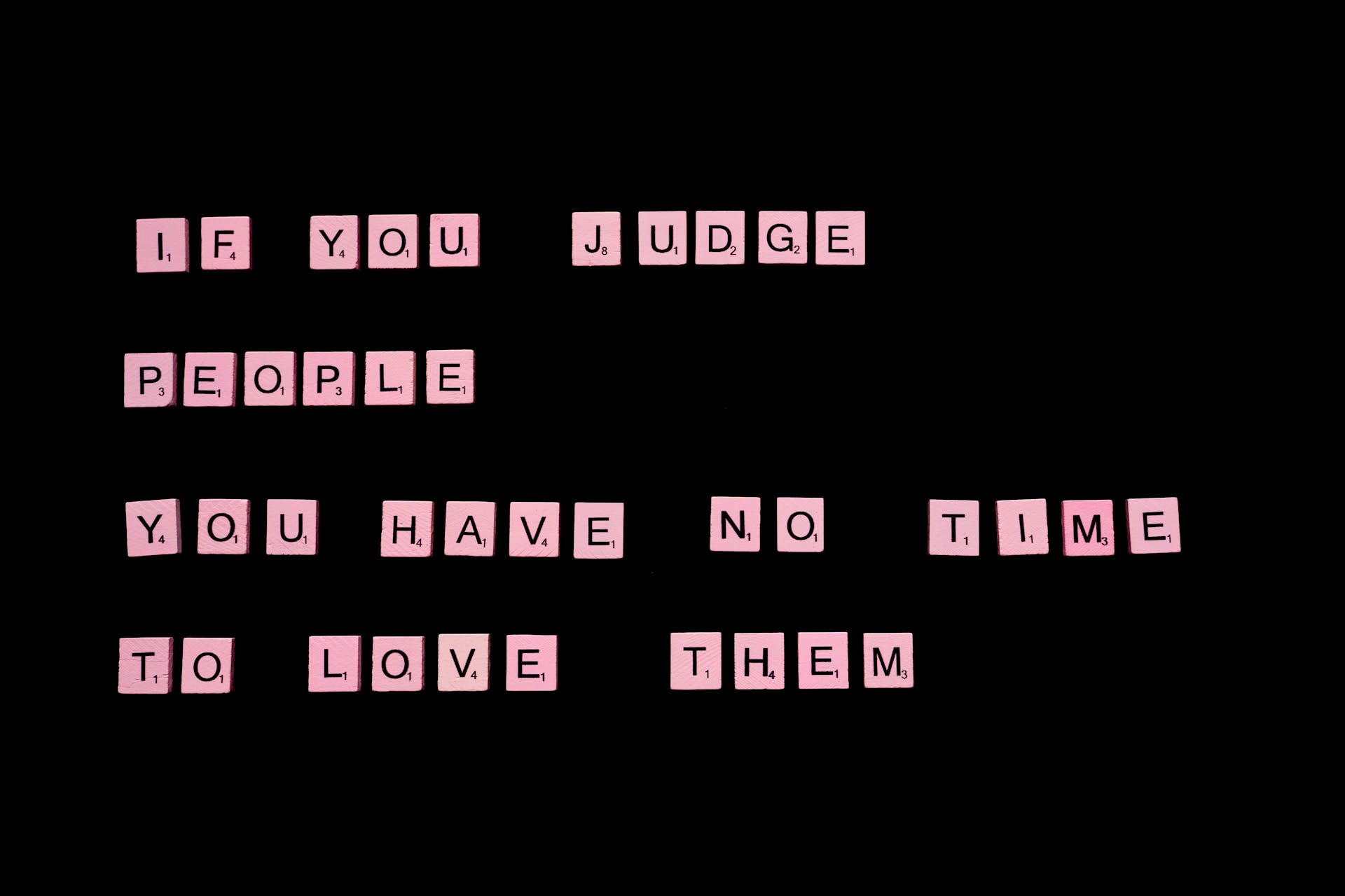 If You Judge People You Have No Time To Love Them text spelled out with pink letter tiles of famous word game against black background