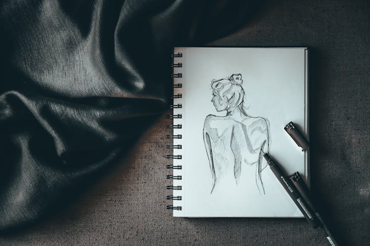 Spiral Sketchbook With Drawn Female Placed On Table