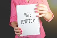 一位穿着粉红色衬衫的女子拿着笔记本，上面写着“度过美好的一天”，传达出积极的态度