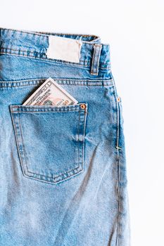 Close-up of blue denim jeans with US dollars in the back pocket, highlighting financial concept.