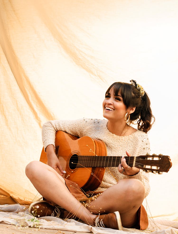 Delighted Young Ethnic Female Musician Playing Guitar On Beach