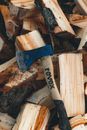 High angle of ax with wooden handle on heap of cut tree trunks with rough bark
