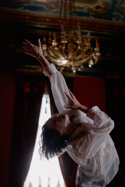 Graceful dancer in elegant attire captured mid-performance under a chandelier.