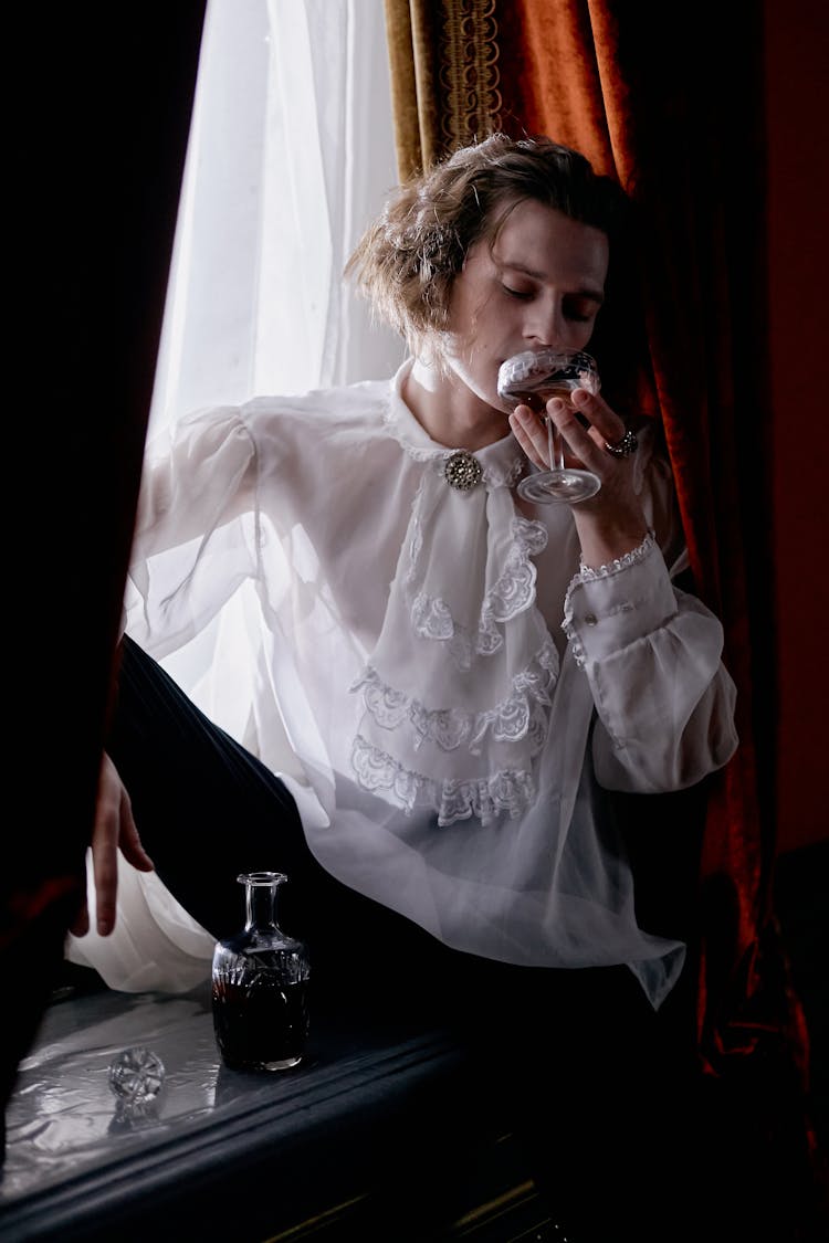 A Man In Renaissance Clothing Sitting On Window Sill Holding A Glass Of Wine