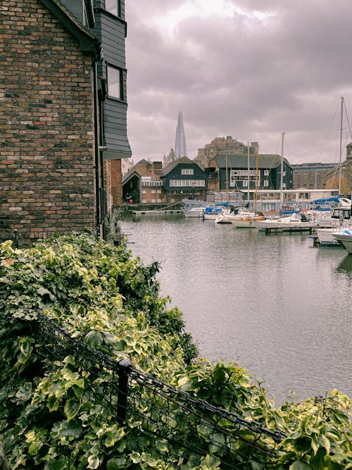 Sailing boats moored on pier of rippling river surrounded by residential buildings under overcast sky