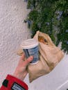 Person with takeaway coffee and bakery in paper bag