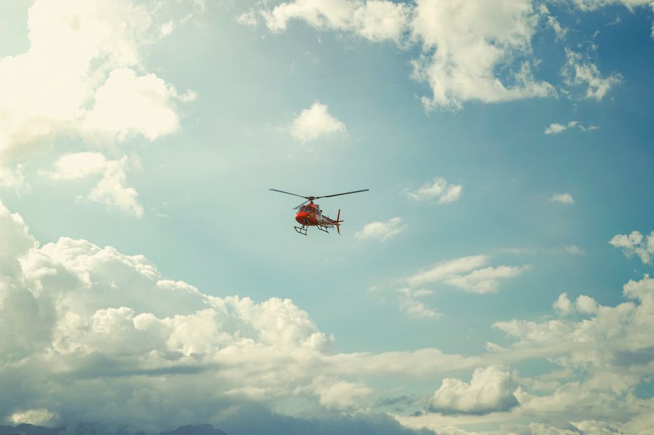 Photo by Francis Seura A vibrant red helicopter soars through a serene sky filled with scattered clouds.