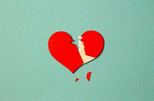 A torn red paper heart on a blue background symbolizes broken love or heartache.