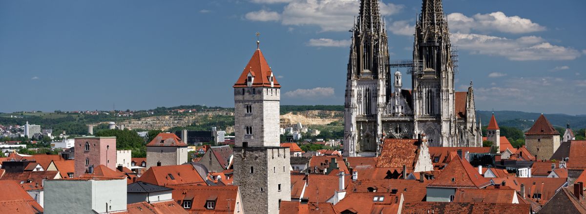 Scenic view of Regensburg's rooftops and Gothic cathedral spires under a blue sky.