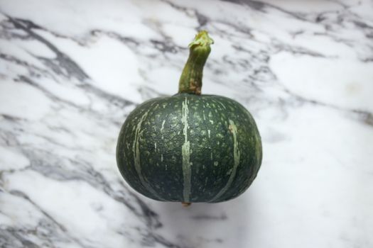 Green pumpkin on marble surface, perfect for autumn or culinary themes.